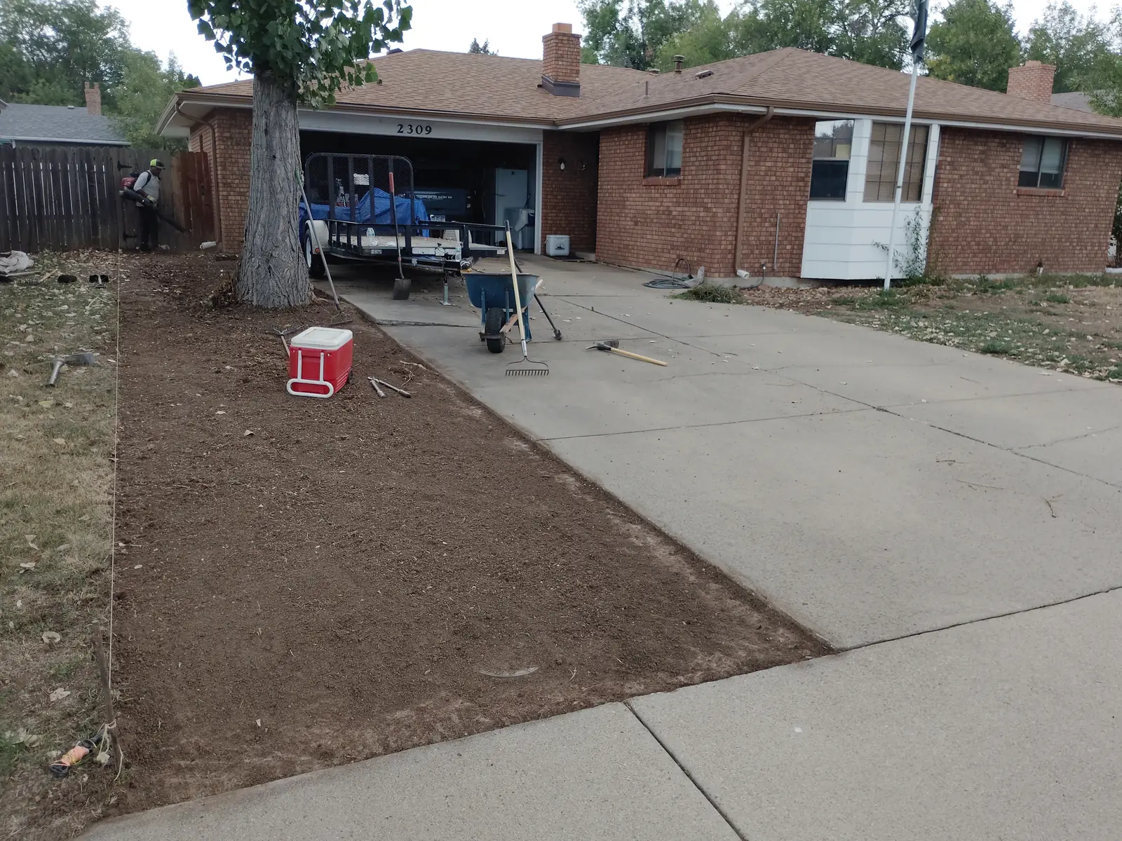 Prep detail: tools, blue wheelbarrow and cooler on the driveway; soil exposed