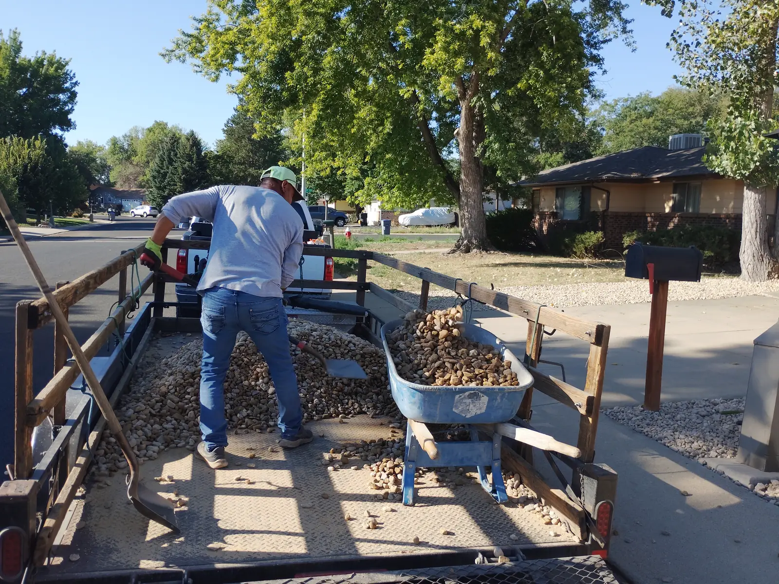 Hauling stone: worker shoveling river rock from the trailer into the blue wheelbarrow