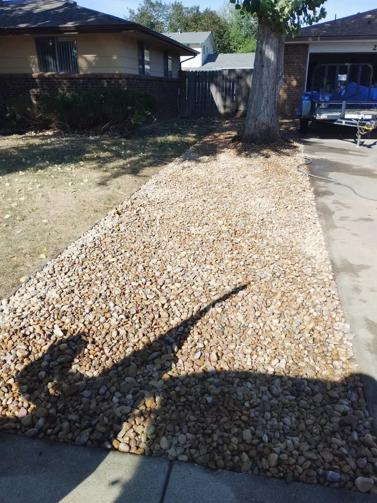 Finished front yard: dense, even layer of natural river rock under a clear blue sky